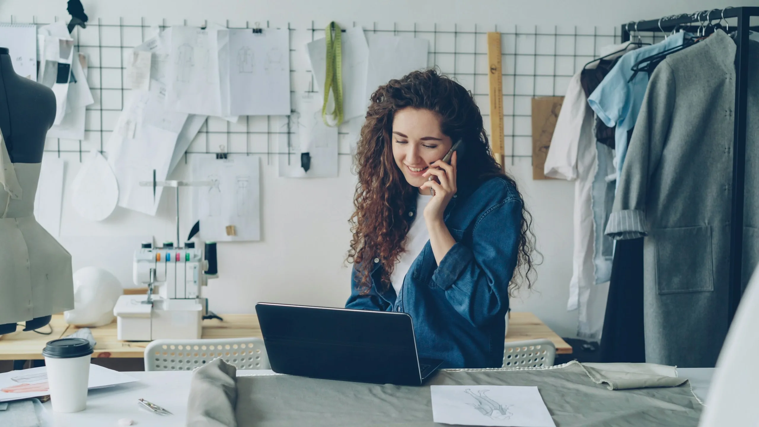 Une créatrice au téléphone, devant son ordinateur portable, dans son atelier de couture