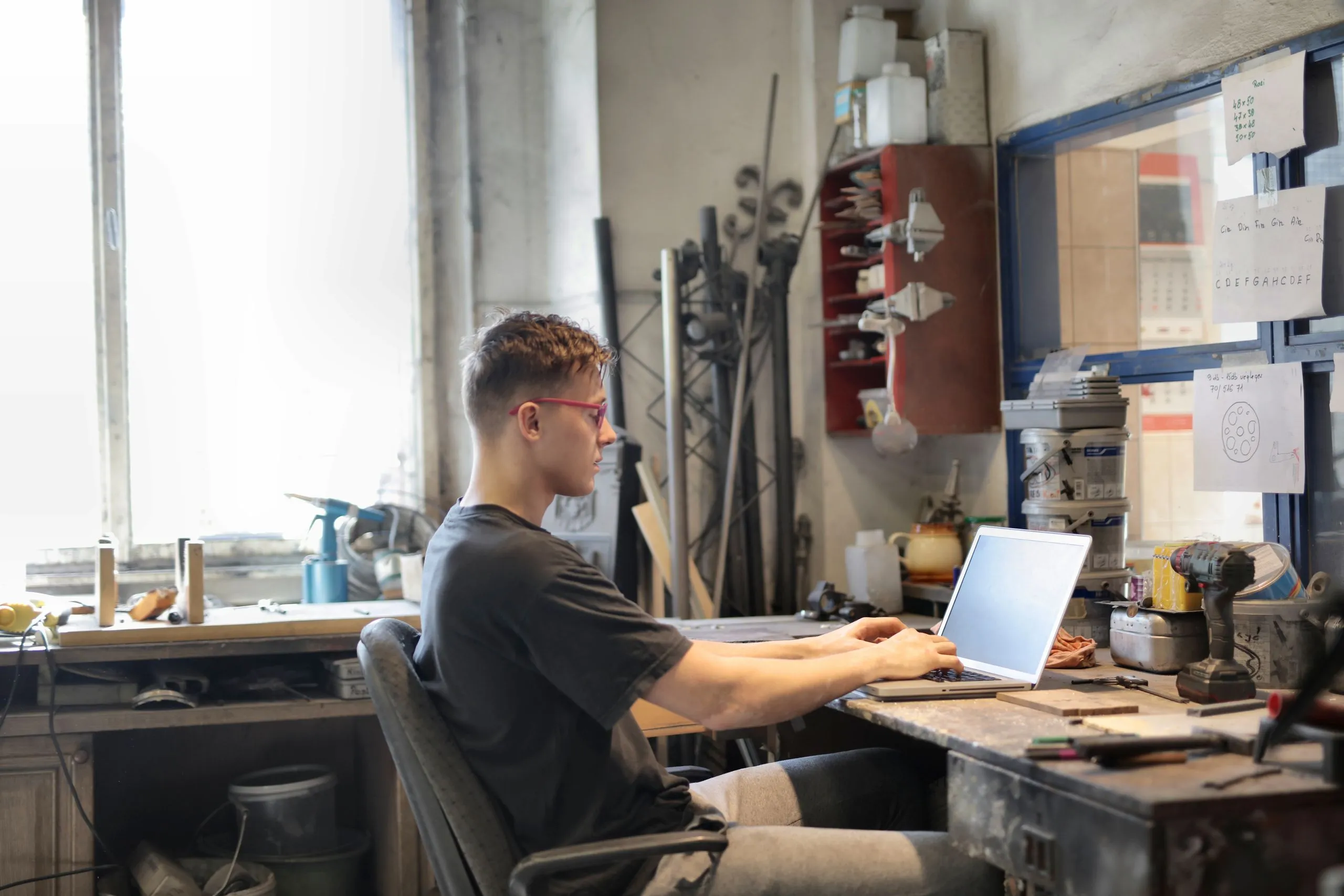 Un artisan tape sur son ordinateur portable dans son atelier, entouré d’outils et de matériel