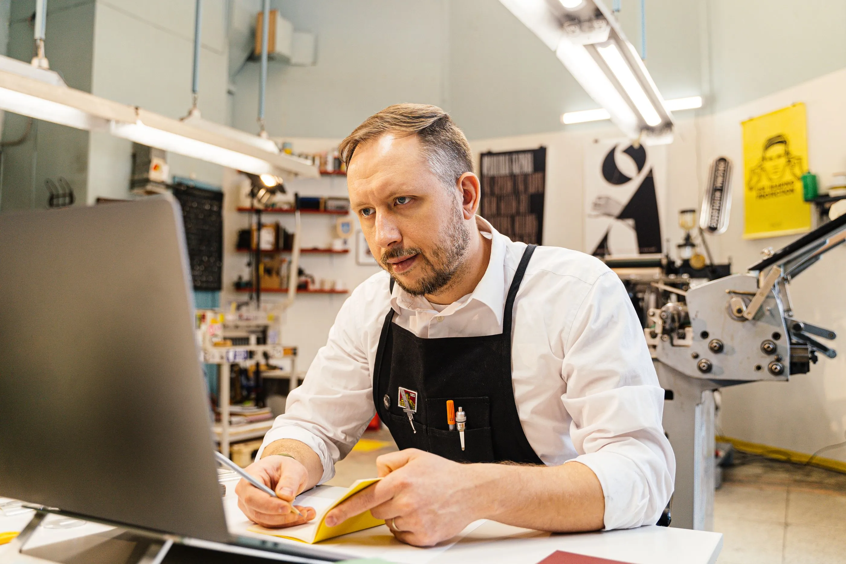 Un artisan imprimeur en tablier consulte son site sur ordinateur dans son atelier